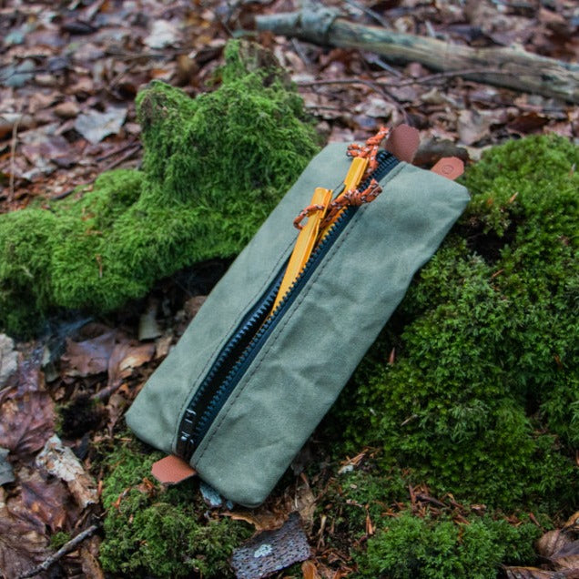 A green canvas peg pouch with tent pegs inside