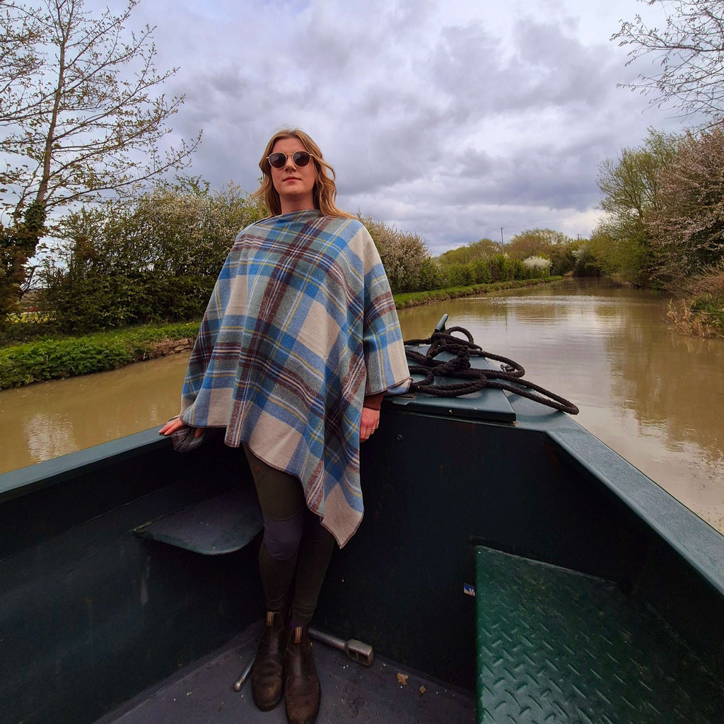 Woman wearing a cozy wool poncho on a boat by a serene canal, showcasing stylish warmth and comfort.