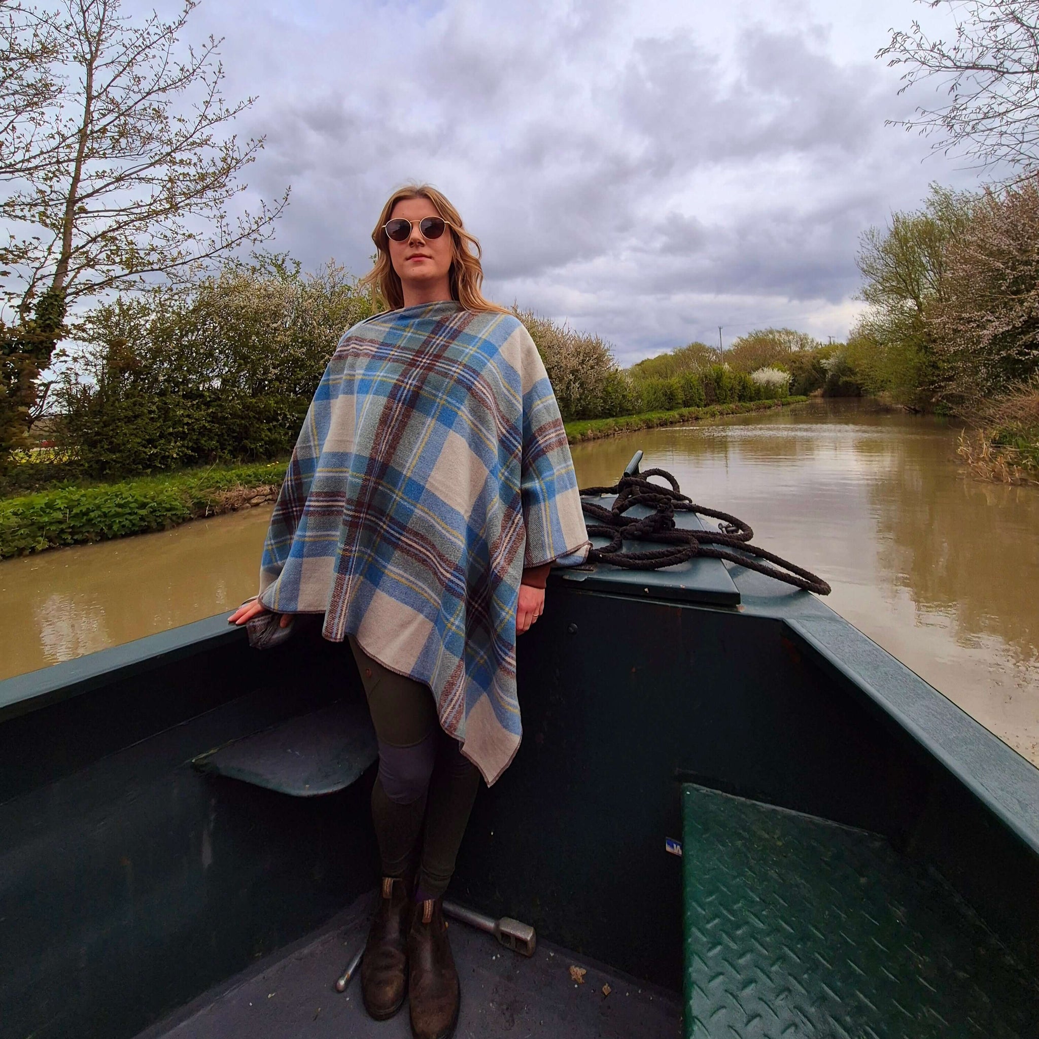 Woman wearing a cozy wool poncho on a boat by a serene canal, showcasing stylish warmth and comfort.