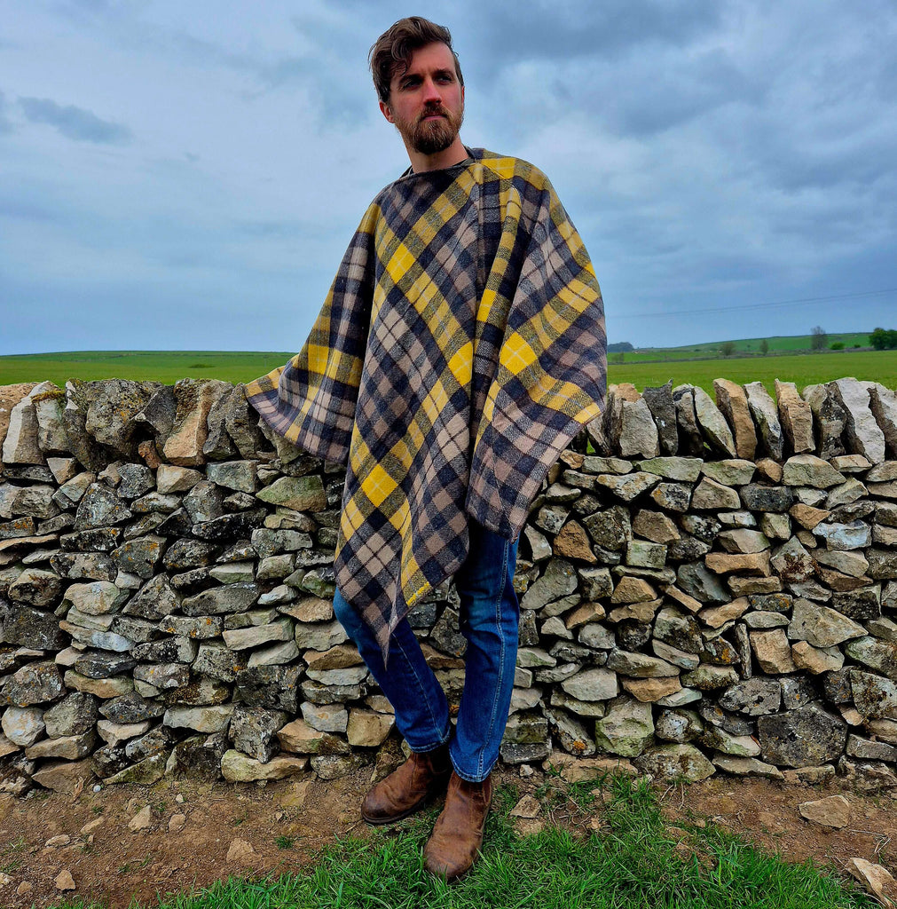 A man wearing a plaid wool poncho standing by a stone wall, showcasing warmth and style in an outdoor setting.