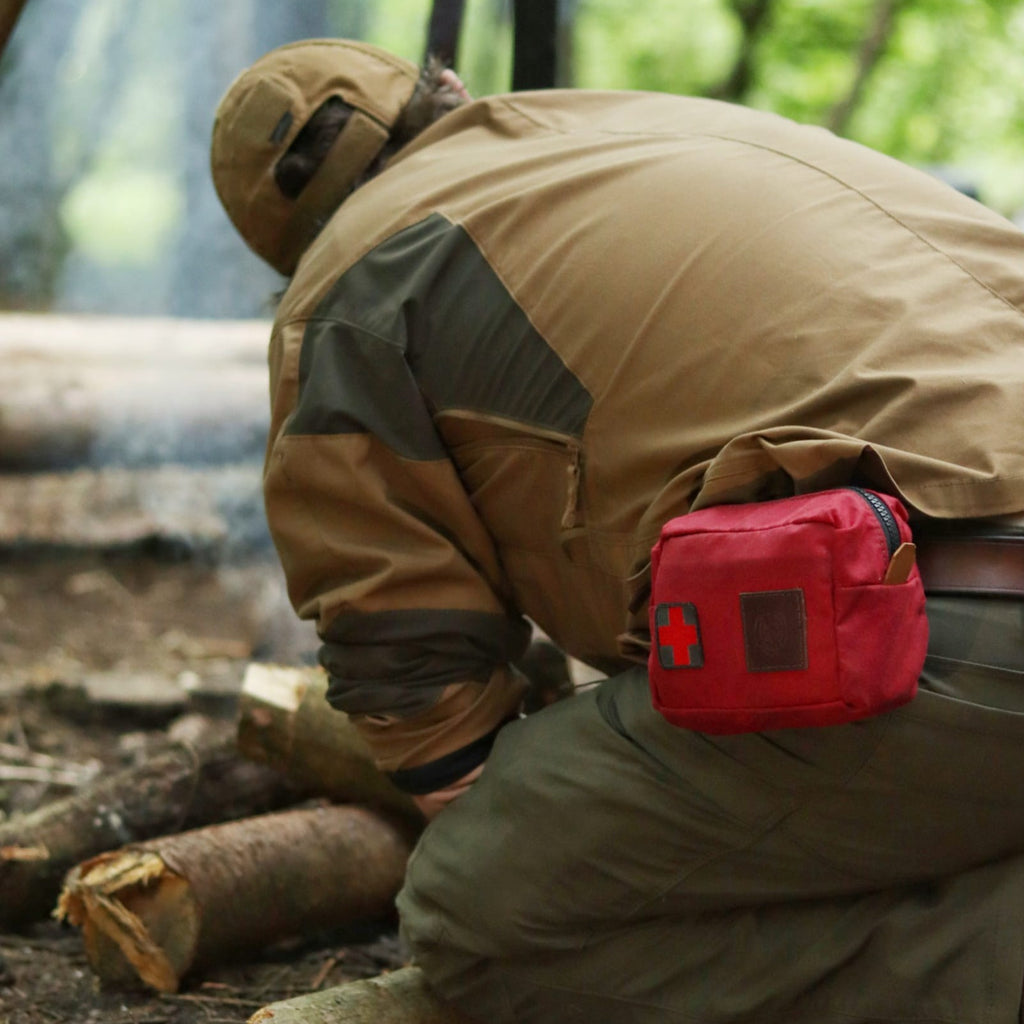A man in the woods practicing bushcraft wearing a red traditional wax canvas first aid kit belt pouch