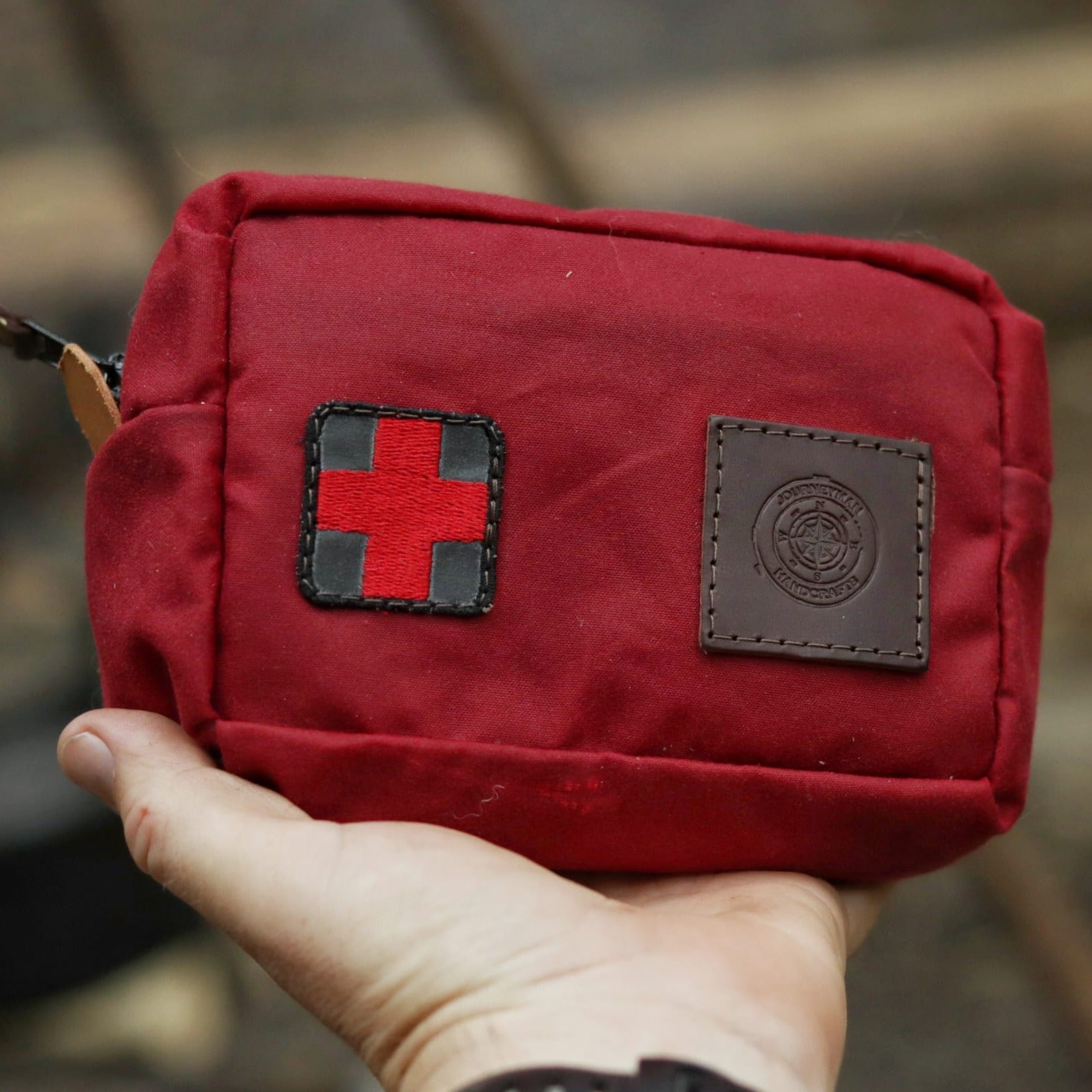 A red traditional wax canvas first aid kit belt pouch with a red cross and leather patch