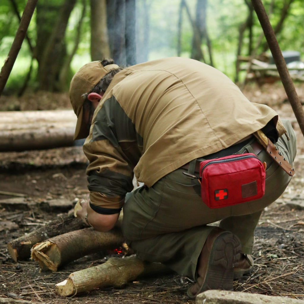 A man in the woods practicing bushcraft wearing a red traditional wax canvas first aid kit belt pouch