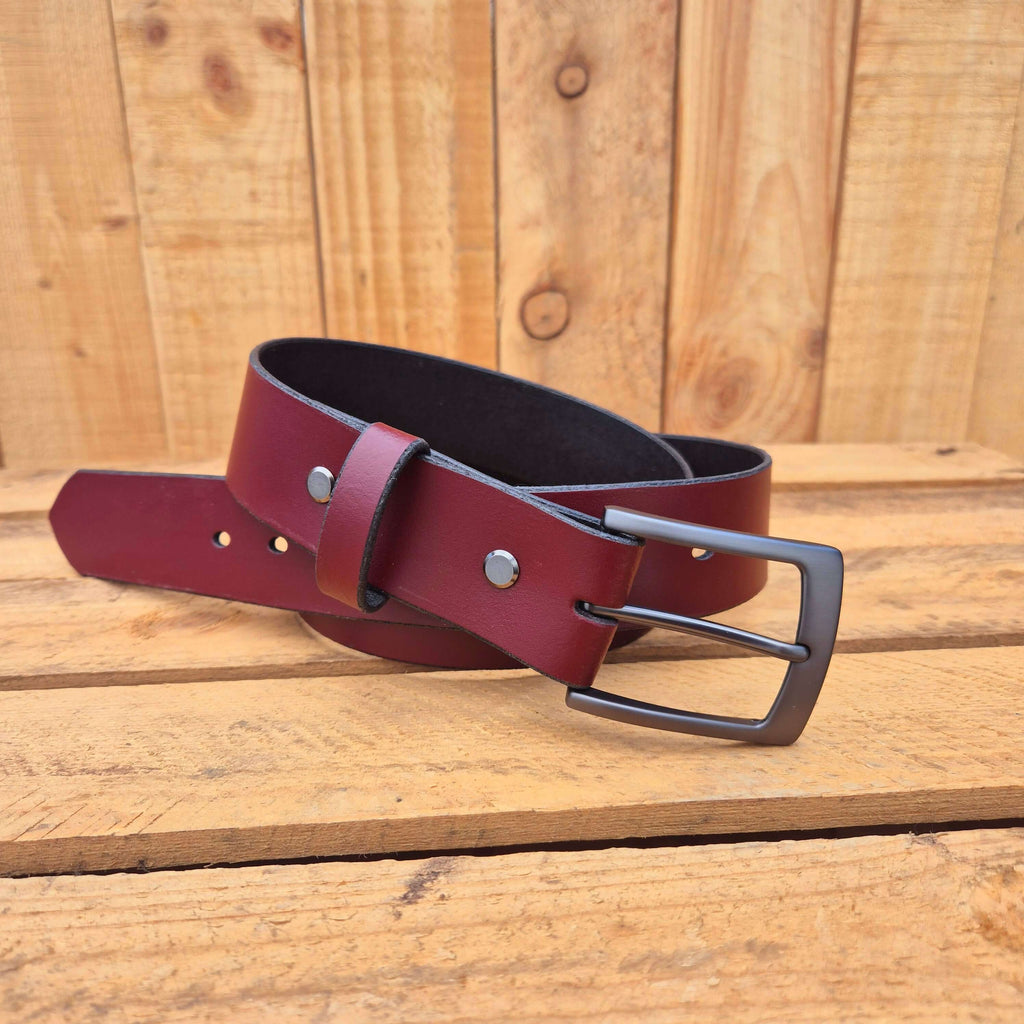 Oxblood leather belt with black buckle on wooden background, showcasing premium craftsmanship and style.