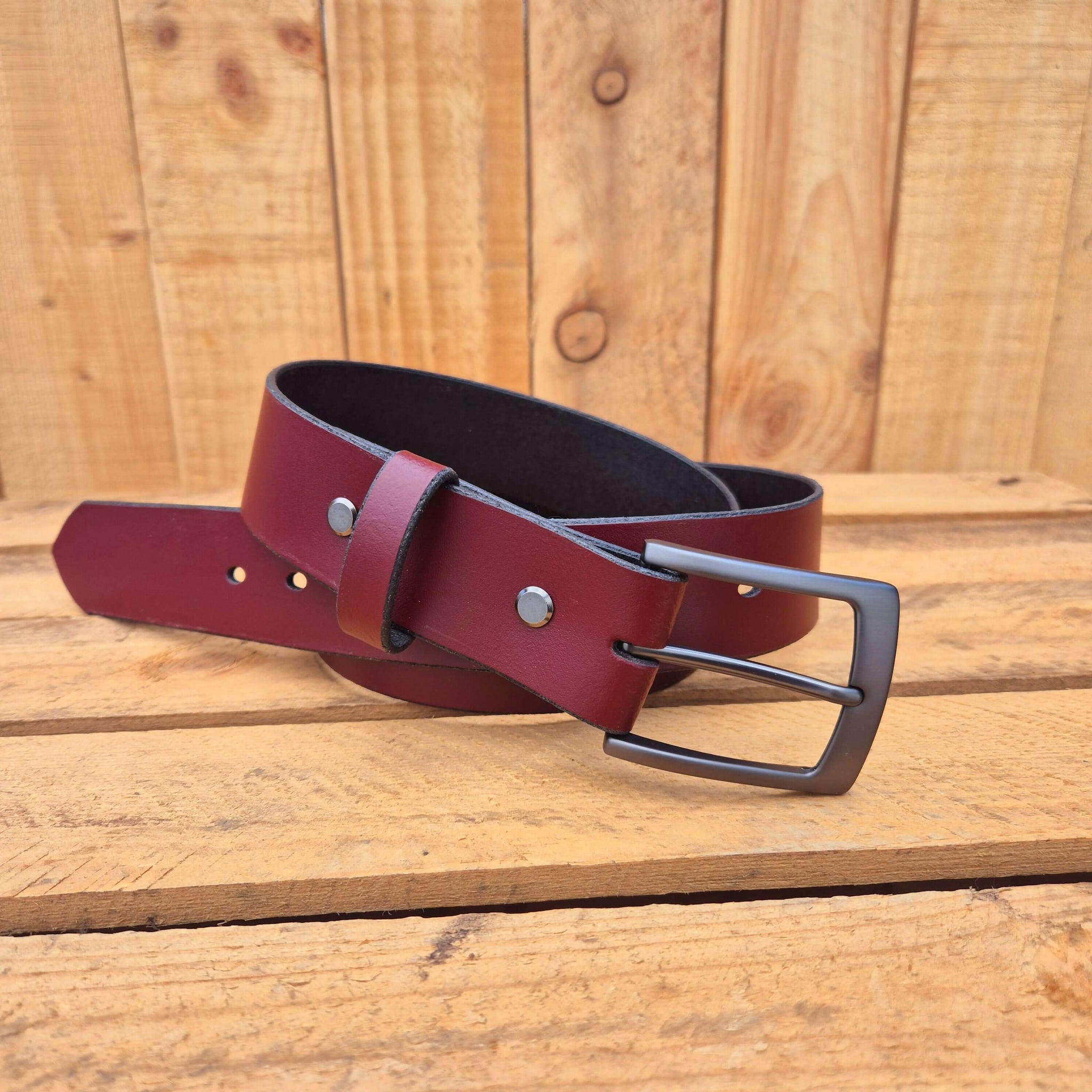 Oxblood leather belt with black buckle on wooden background, showcasing premium craftsmanship and style.