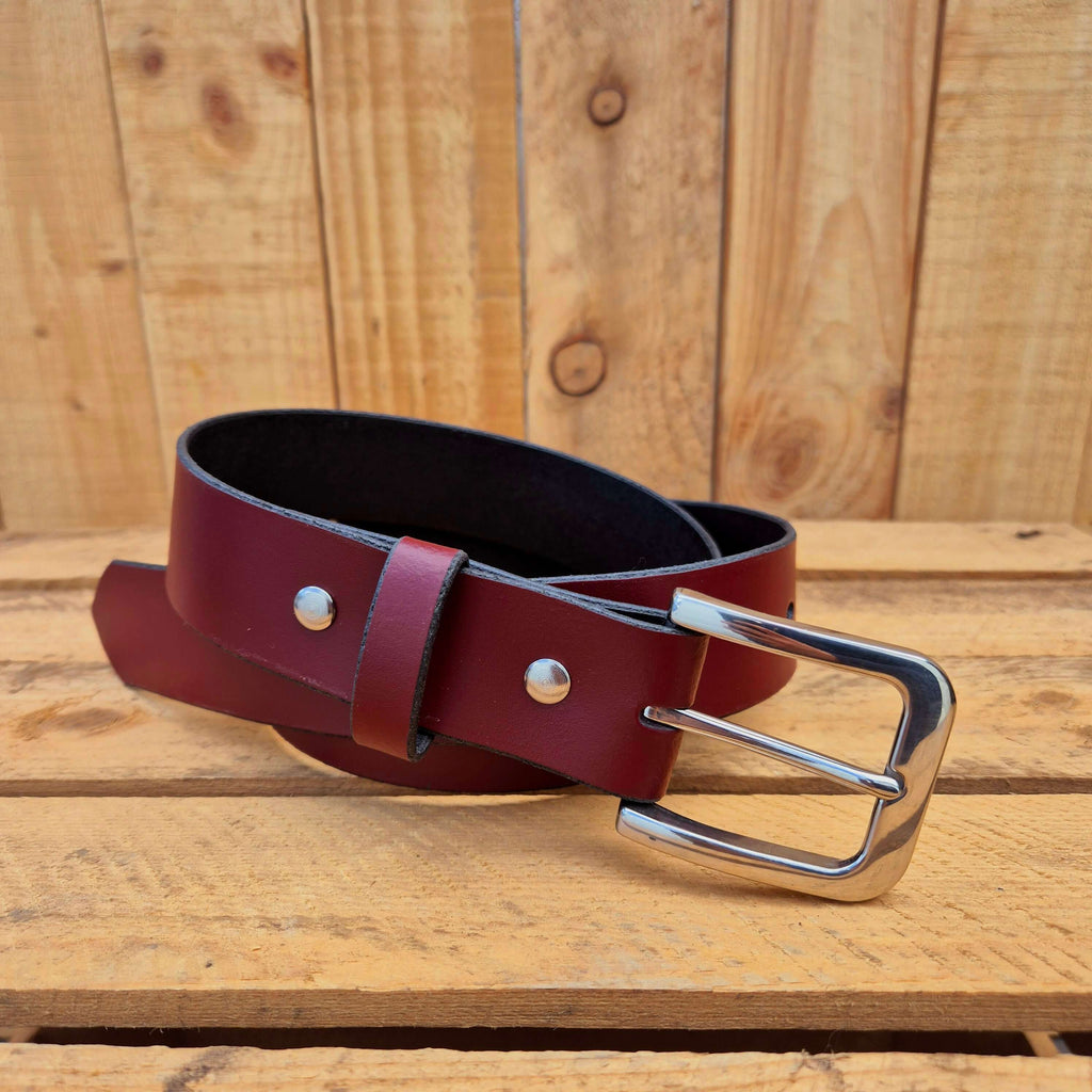 Oxblood leather belt with silver buckle on wooden background, showcasing craftsmanship and style.