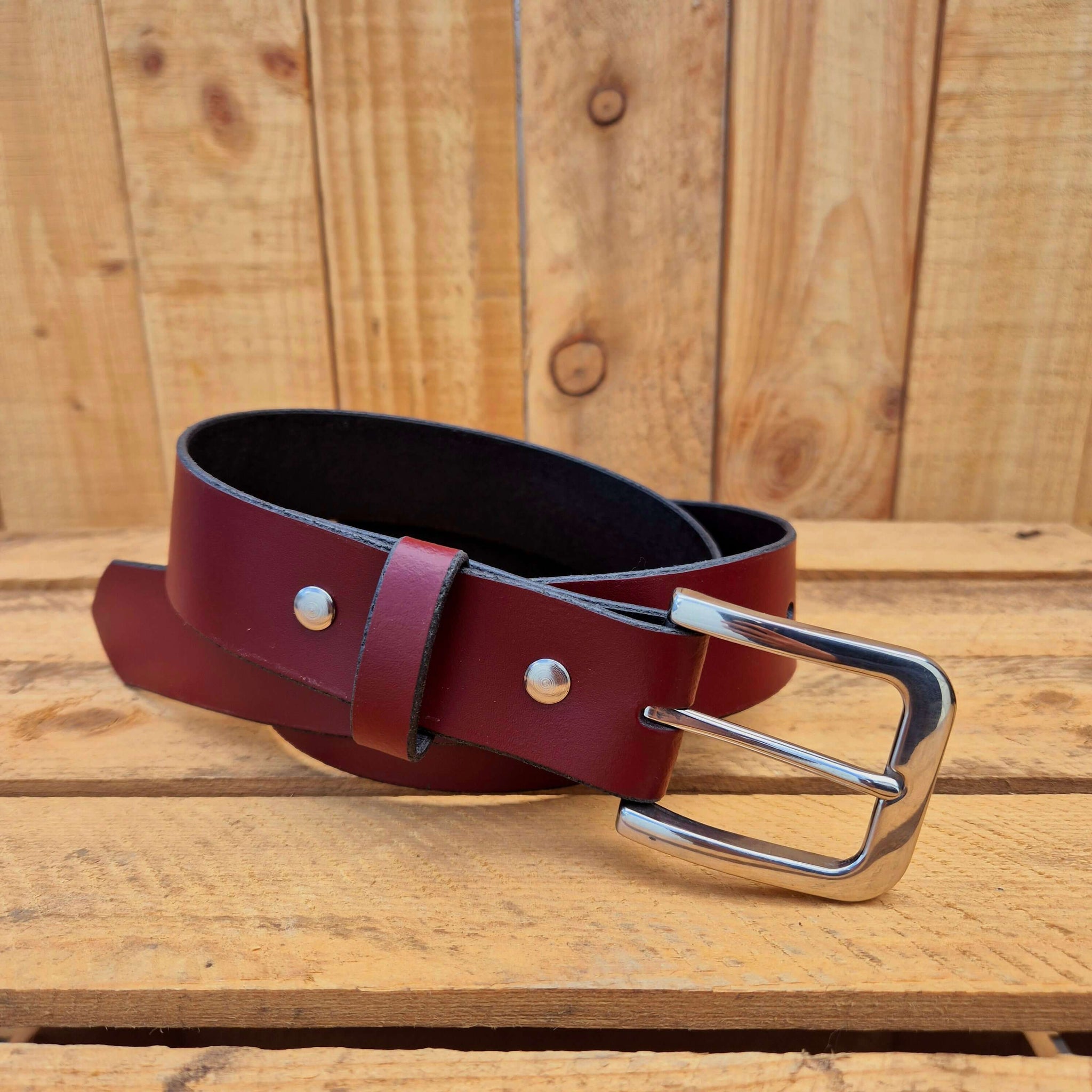 Oxblood leather belt with silver buckle on wooden background, showcasing craftsmanship and style.
