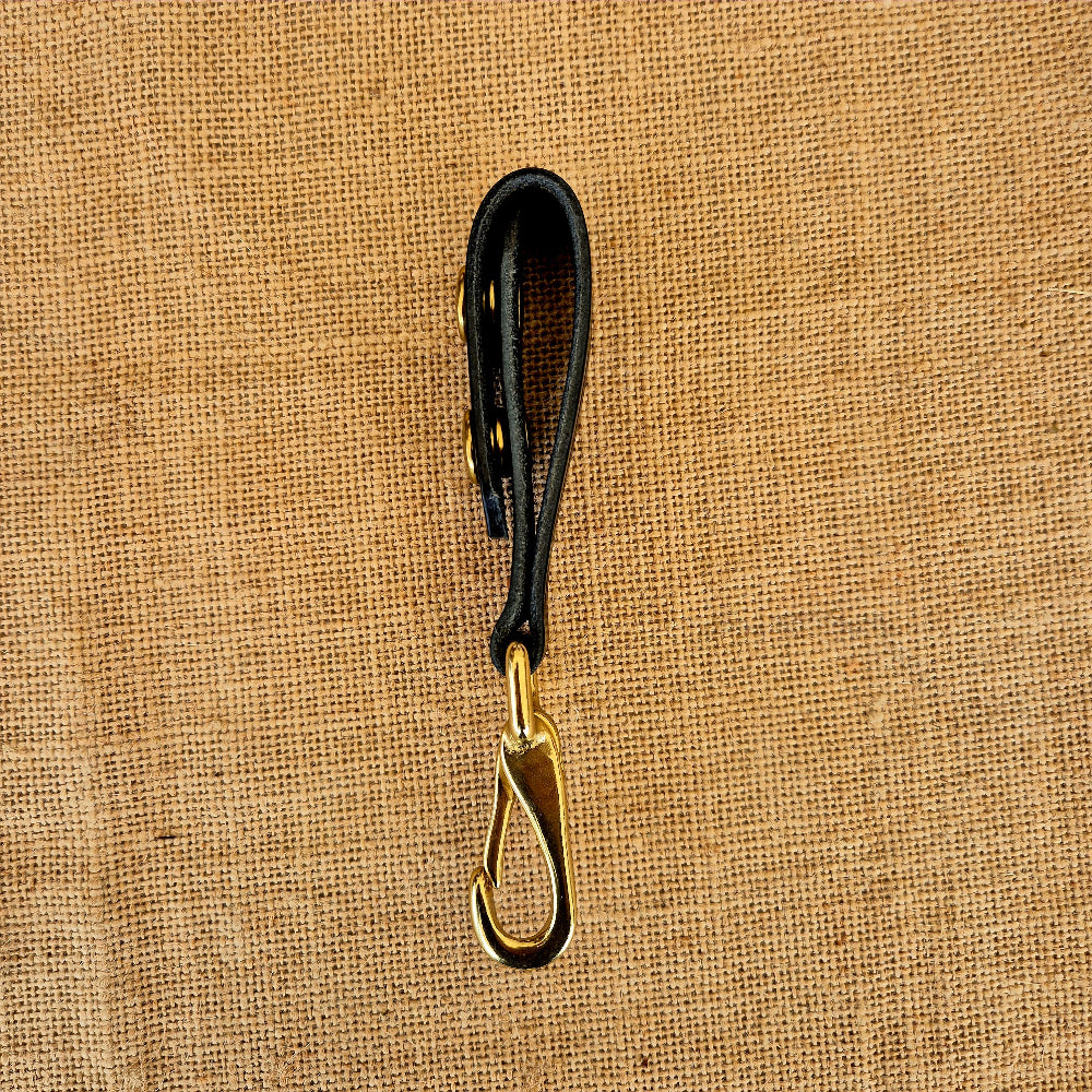Black leather keychain with gold clasp on a beige fabric background