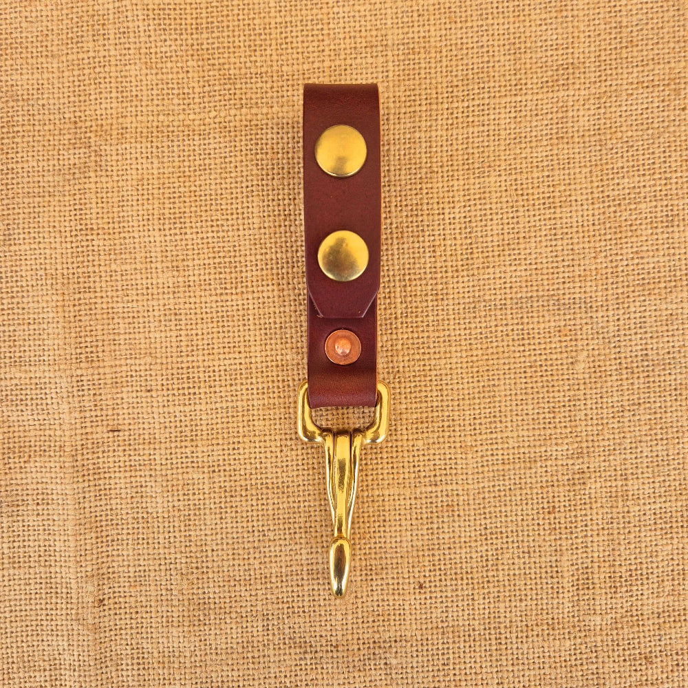 Brown leather strap with brass snap buttons and a gold clip, laid on burlap background.