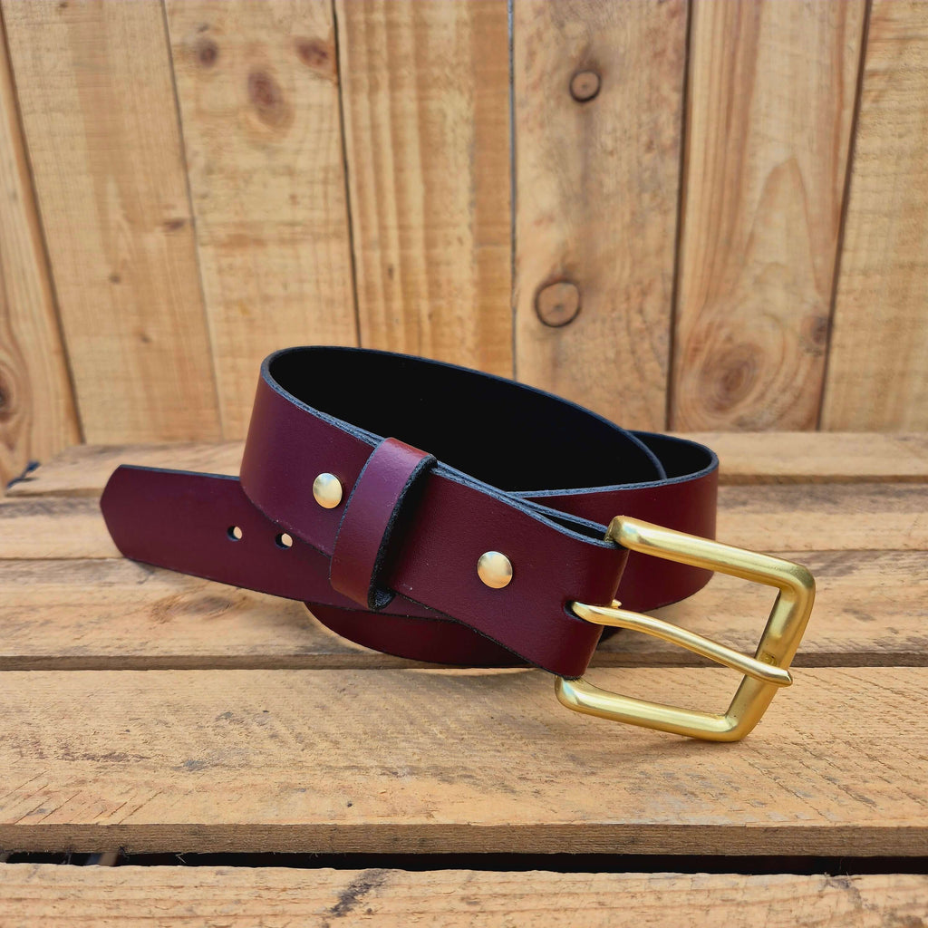 Oxblood leather belt with gold buckle on wooden background, showcasing premium craftsmanship.