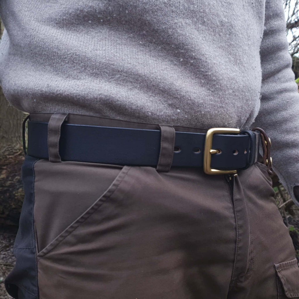 A man wearing a hand made black leather belt with a brass buckle