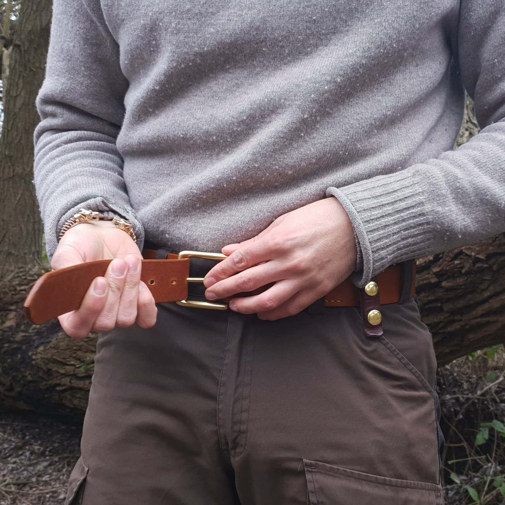 Man putting on a tan brown leather belt with brass buckle