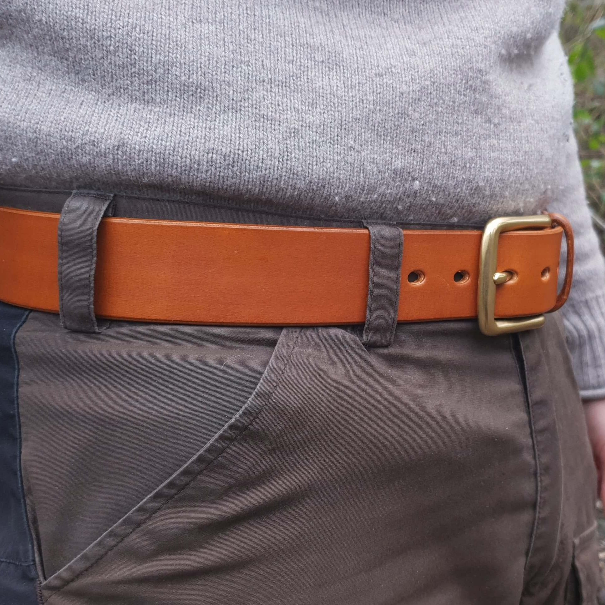 A tan brown leather belt with a brass buckle